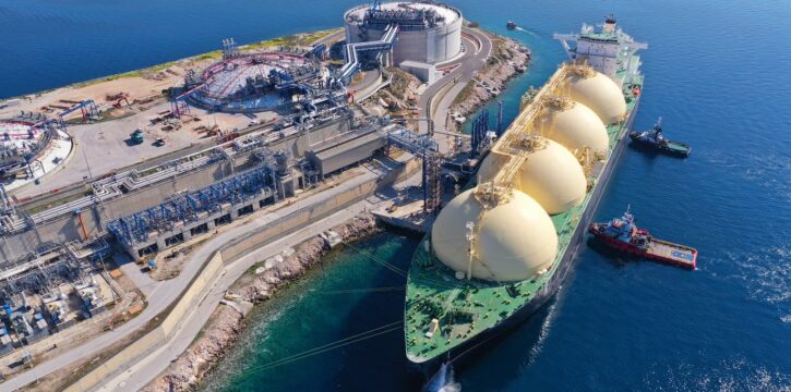 A wide landscape shot of the Ras Laffan LNG export terminal in Qatar showing industrial storage tanks and processing units under a clear sky.