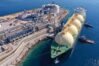 A wide landscape shot of the Ras Laffan LNG export terminal in Qatar showing industrial storage tanks and processing units under a clear sky.